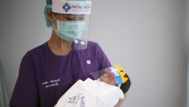 Un sanitario junto a un bebé con mascara por el covid-19.