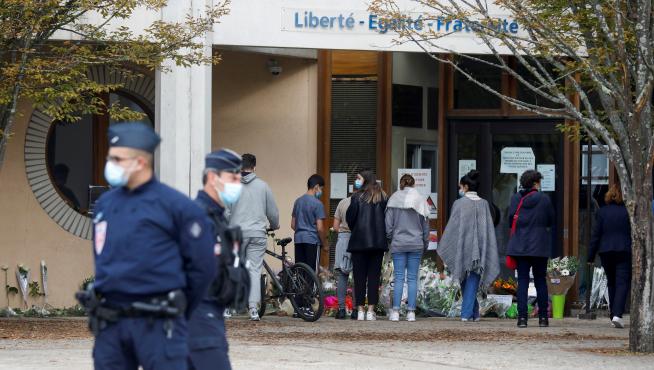 Varias personas depositan flores en la entrada del colegio donde daba clase el profesor asesinado.