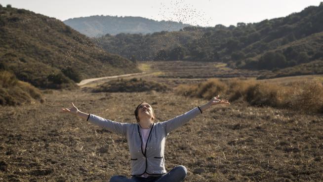 Ana Marcén, sentada sobre el rastrojo en un campo de Leciñena, lanza al aire semillas del trigo Aragón 03 que ha recuperado.