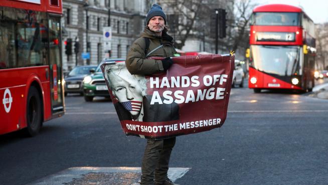A man rides a skateboard holding a banner with an image of Julian Assange in London, Britain, December 30, 2020. REUTERS/Hannah McKay[[[REUTERS VOCENTO]]] BRITAIN-ASSANGE/