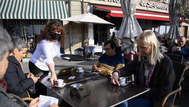 Un camarero con mascarilla sirve cafés a varios clientes en la terraza de un restaurante de Nyon. En Suiza los interiores de los bares siguen cerrados.