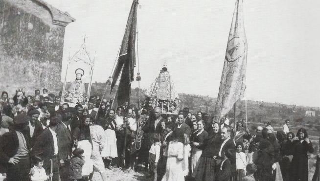 El pueblo de Sariñena, de todas las edades, asiste a la procesión del año 1934, con banderas y santos identificados en la imagen.