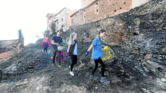 Un grupo de jóvenes limpian la zona quemada en Moros, que llegó a las puertas de los locales de las peñas.