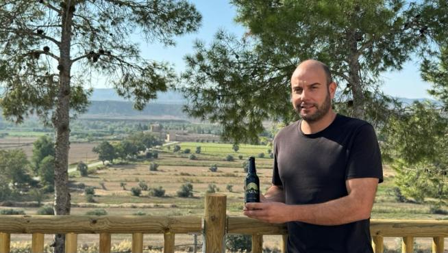 José Jaime Castellón posa con la nueva cerveza Sixena. Al fondo, el monasterio