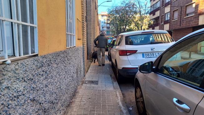 Un hombre pasea con su perro por la calle de Cariñena, cuya acera mide unos 90 centímetros de ancho.