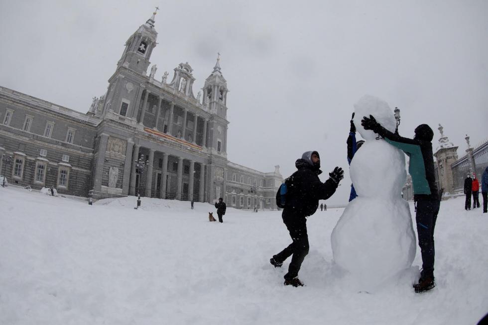 Dos personas hacen un muñeco de nieve en las inmediaciones de la Catedral de la Almudena, en Madrid.