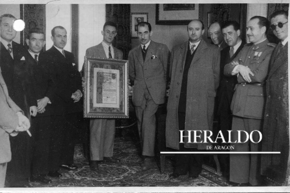 Se cumplen 70 años del ofrecimiento al gobernador civil, don Tomás Romajaro, de parte de una comisión municipal de Olmedo (Valladolid), presidida por su alcalde don Gregorio Santiago, de un pergamino en el que consta el acuerdo del Ayuntamiento de Olmedo de poner el nombre del actual gobernador civil de Zaragoza, anteriormente de Valladolid, a un grupo escolar en construcción en aquella localidad. Estuvieron presentes el presidente de la Diputación, señor García Belenguer, el subjefe provincial del Movimiento don Juan José Sarto Ibarra, diputado provincial don Miguel Mermo Esquerro, delegado provincial de ex cautivos, don Arturo Guillén Urzáiz, secretario local del Movimiento, teniente coronel Rodríguez Pérez, delegada provincial de la Sección Femenina, Ofelia Díaz, delegado provincial de Auxilio Social, don Joaquín Mateo Linares, inspector provincial del Movimiento, señor Pérez Enciso, y otros jefes de servicios. La comisión de Olmedo que presidia el alcalde, la integraban don Eusebio Valero, don Alejandro García y don Luis Martínez. En la imagen, el gobernador en su despacho el 18 de febrero de 1948, con los asistentes.