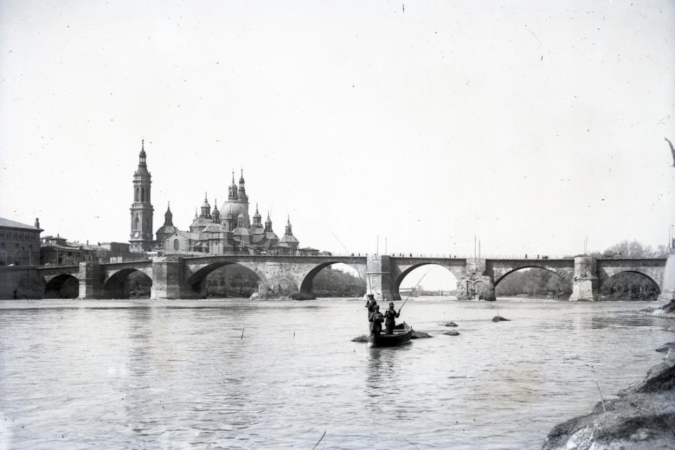 Unos pescadores surcan las aguas del Ebro con la Basílica y sus dos torres en la década de los 20