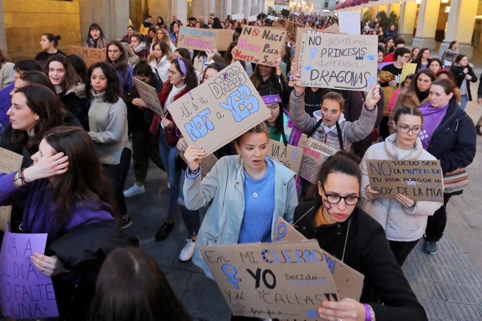 Jóvenes con carteles reivindicativos al paso de la manifestación por los porches de Galicia