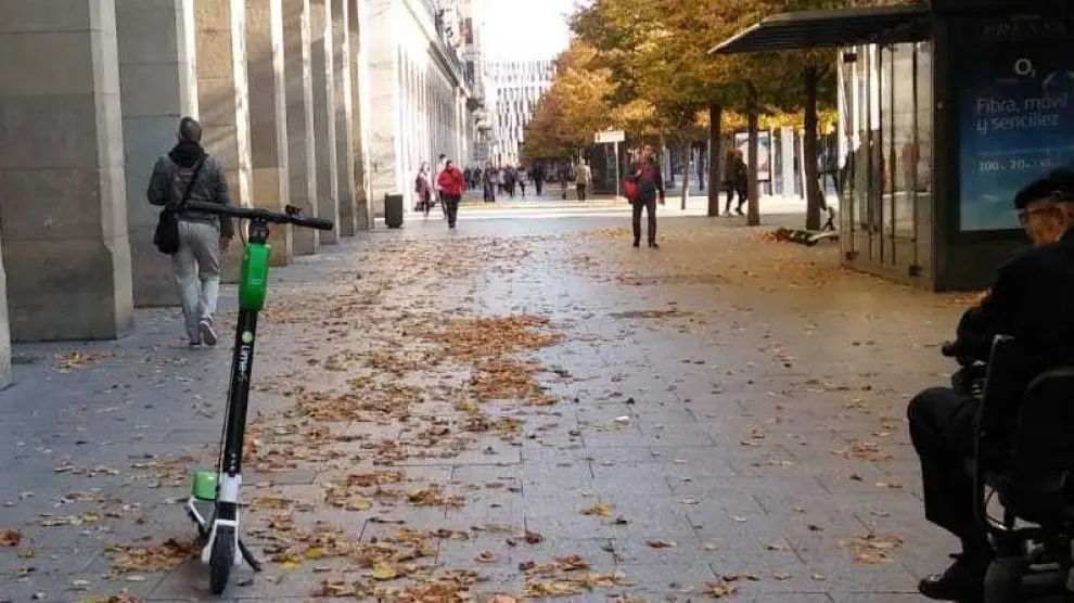 Un hombre en silla de ruedas mira un patinete eléctrico de alquiler abandonado en plena acera, en el paseo de Independencia de Zaragoza este lunes.