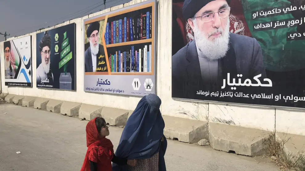 Una mujer con burka y una niña pasan por un muro con publicidad electoral del señor de la guerra Gulbudin Hekmatyar