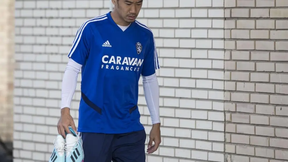 Shinji Kagawa, camino del gimnasio con las botas en la mano, con gesto torcido.
