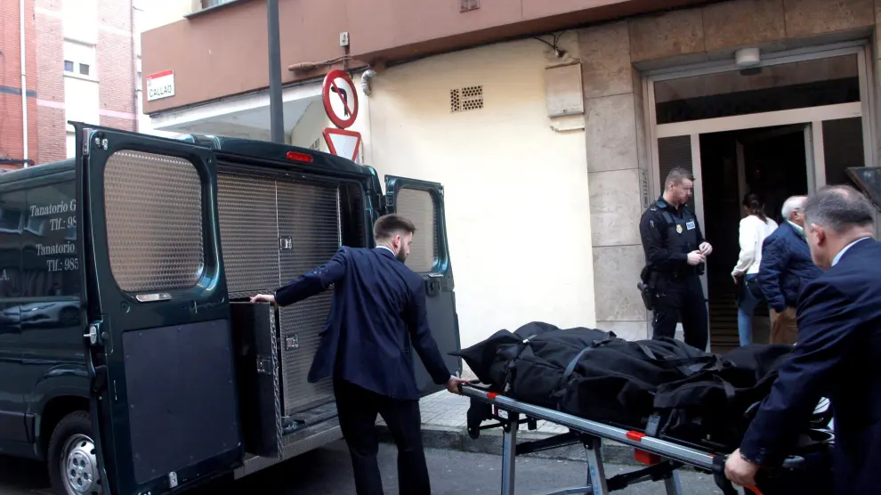 Dos personas trasladan el cadáver de una mujer de 41 años, hallado este lunes por la Policía Local de Gijón con evidentes signos de violencia en su domicilio
