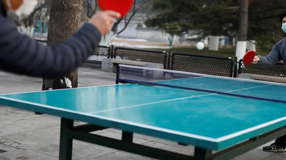 Dos personas con mascarilla juegan al tenis de mesa en un parque de Pekín
