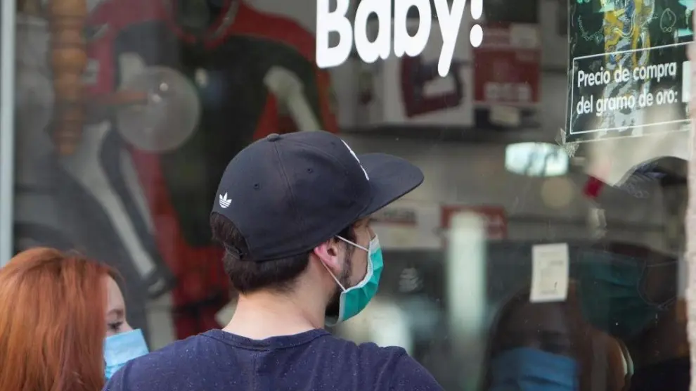 Dos ciudadanos con mascarillas observan el escaparate de una tienda de empeños.