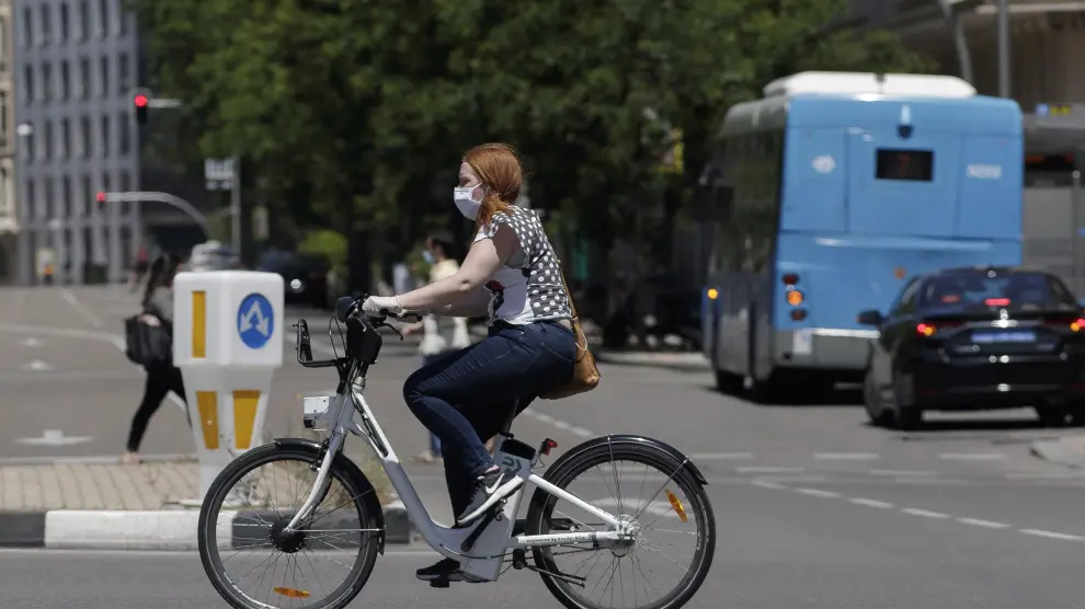 Una mujer protegida con mascarilla monta en una bicicleta.
