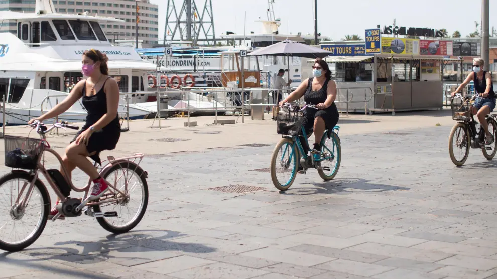 Tres turistas pasean por el puerto de Barcelona con bicicleta.