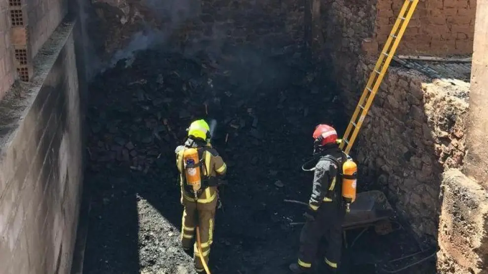 Bomberos sofocando el incendio que se ha producido en un solar que acumulaba leña, en Híjar (Teruel).