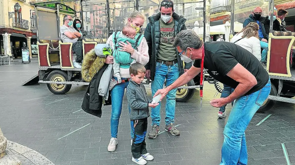 Los turistas limpian sus manos antes de subir al tren turístico en la plaza del Torico de Teruel.