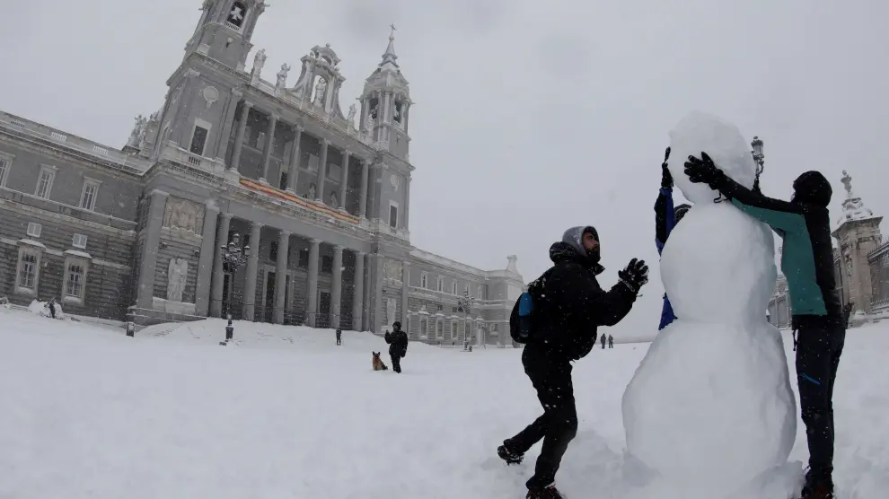 Dos personas hacen un muñeco de nieve en las inmediaciones de la Catedral de la Almudena, en Madrid.
