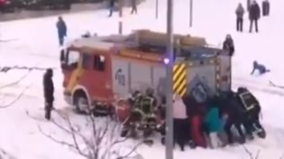 Un grupo de ciudadanos empujan un camión de los Bomberos, atrapado por la nieve en una calle de Madrid.