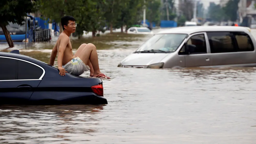 Un joven subido a un coche en una carretera inundada tras las fuertes lluvias en Zhengzhou.
