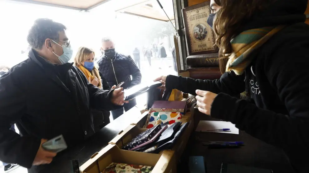 Lucía Pitarch, de Atrapavientos, entrega su libro a un lector que acudió este domingo a la plaza del Pilar