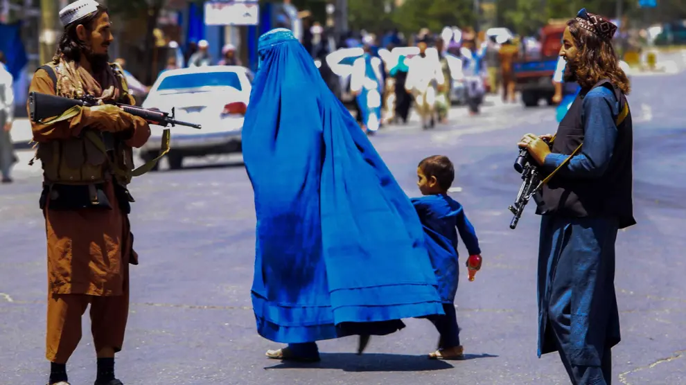 Una mujer con burka pasa junto a centinelas armados en una calle de Kabul.