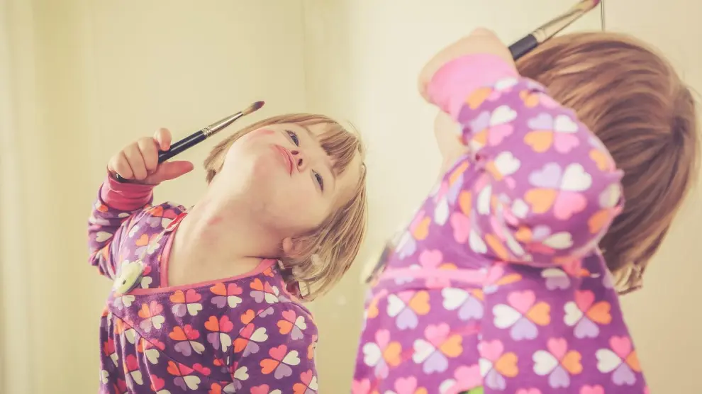 Un niña con síndrome Down juega frente a un espejo.