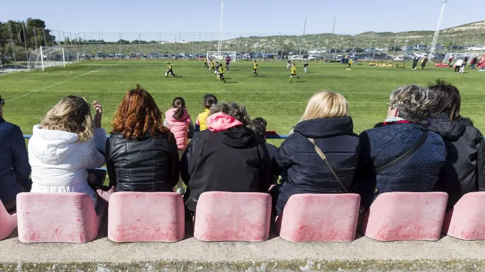 Un partido del fútbol base del Real Zaragoza en la Ciudad Deportiva, observado por padres y madres en las gradas.