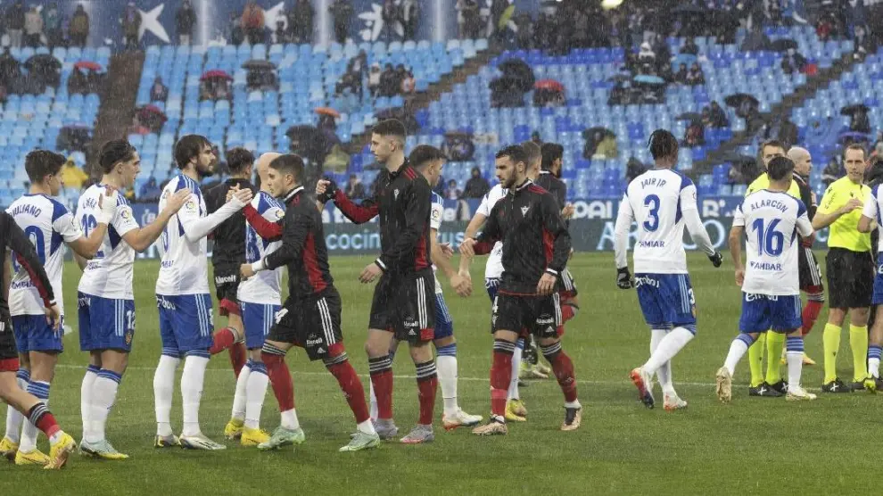 Los futbolistas de ambos equipos se saludan antes del partido, bajo un intenso aguacero sobre Zaragoza.