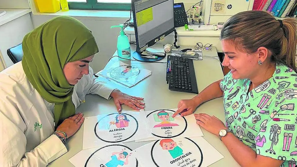 Las enfermeras Umayma Beni Abdellah y Pilar Asión, con algunos de los pictogramas en Caspe