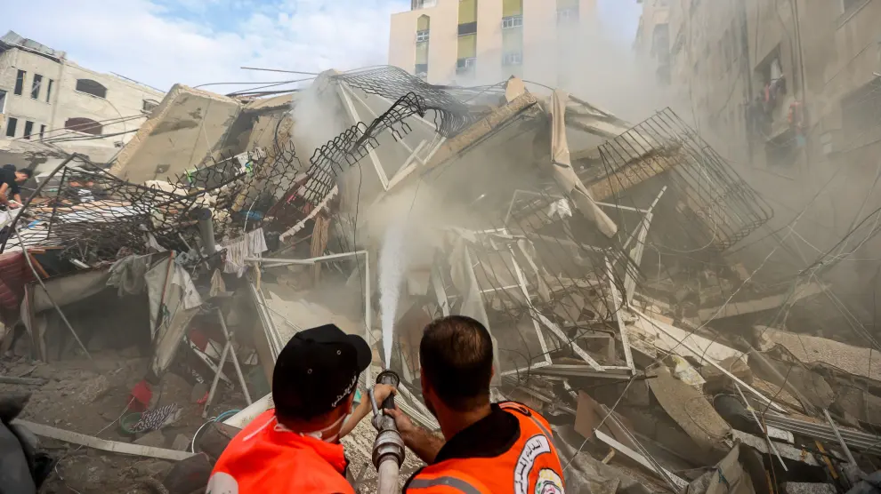 Dos bomberos refrescan los restos de un edificio en ruinas en Gaza