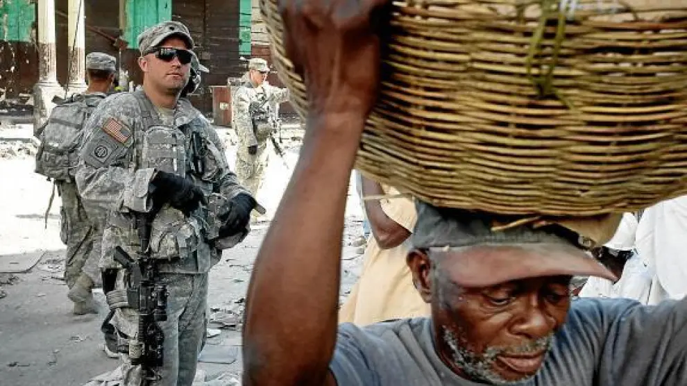 Un haitiano carga con un cesto en Puerto Príncipe ante la mirada de un soldado estadounidense.