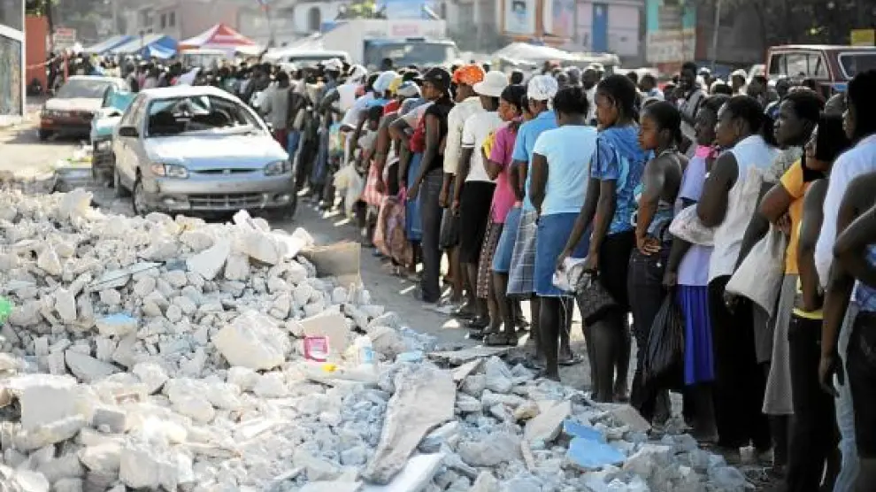 Los haitianos hacen fila para recibir alimentos junto a unos escombros, ayer en Puerto Príncipe