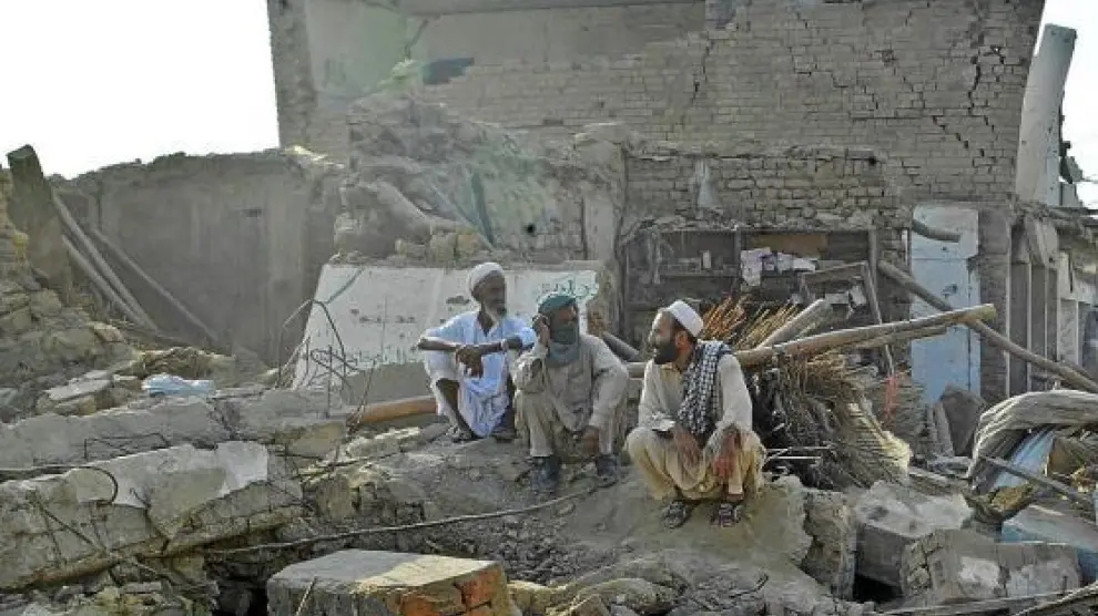 Tres hombres paquistaníes descansan entre las ruinas cercanas al lugar del atentado.