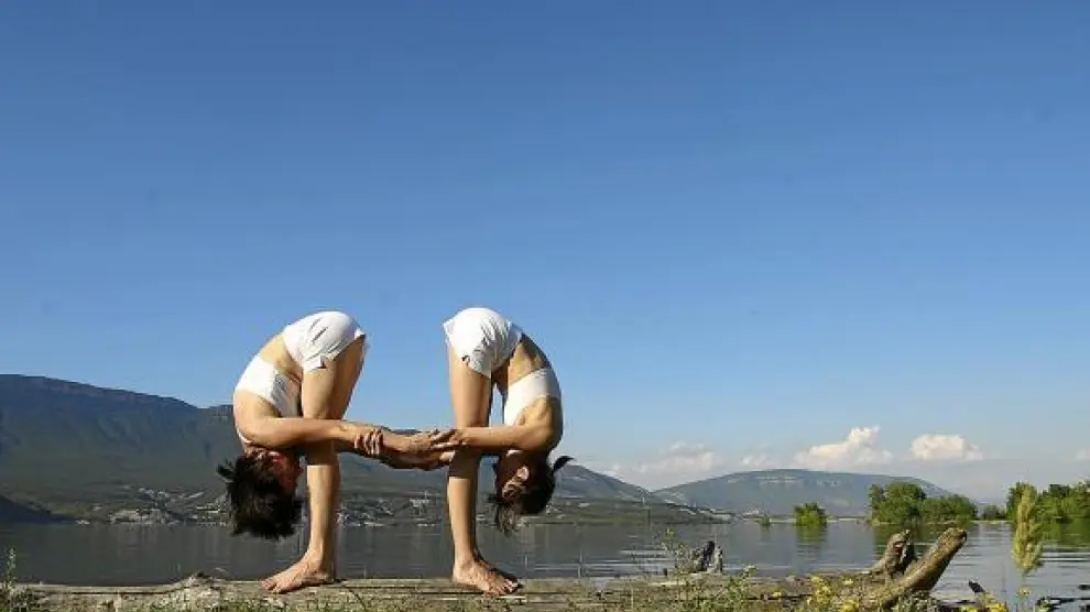 Dos mujeres practican un ejercicio de yoga junto al embalse de Yesa.