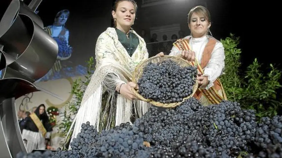 Dos reinas de fiestas, ataviadas con el traje regional, echan las uvas en la portadera.