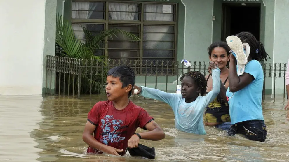 Unos niños intentan cruzar la calle inundada