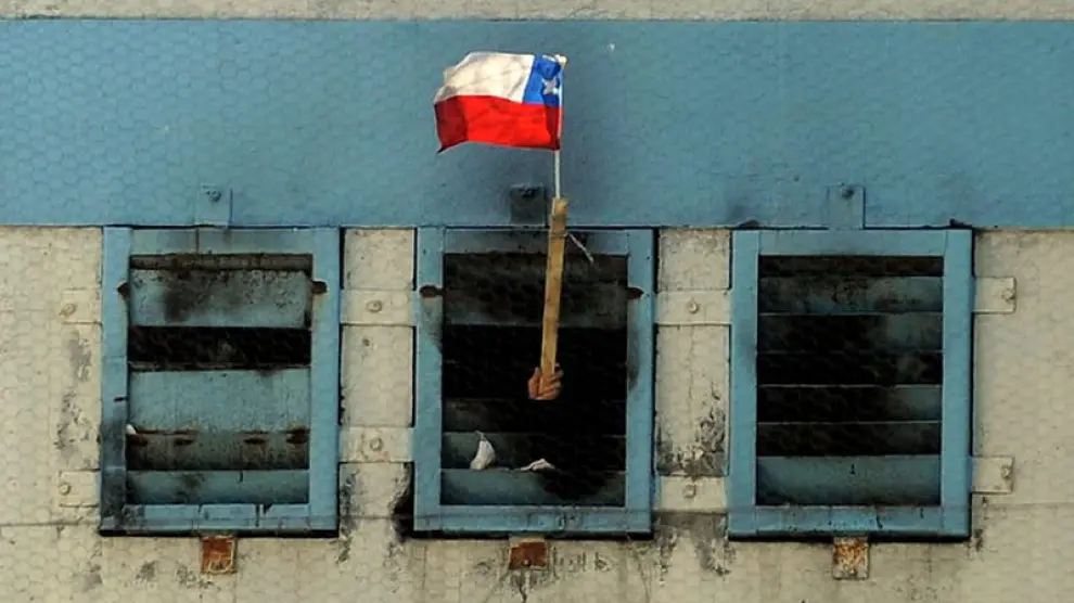 Un interno muestra una bandera chilena desde el interior de la cárcel.