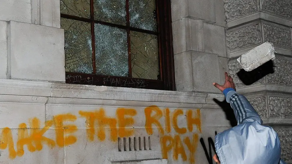 Un joven destroza la ventana de un edificio.