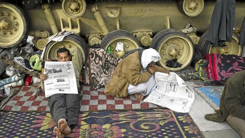 Dos egipcios leen la prensa junto a un blindado en la plaza de Tahrir de El Cairo, ayer.