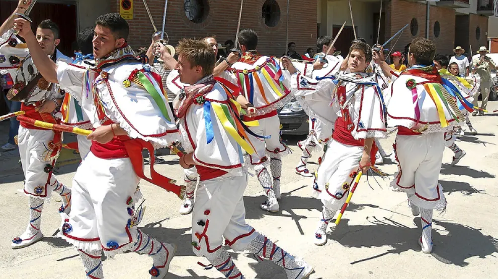 Los danzantes de Tardienta van bailando en el pasacalles que conduce a la imagen y a la bandera a la iglesia parroquial.