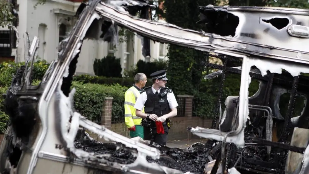 Un policía y un trabajador de la limpieza retiran los escombros de un vehículo en Liverpool