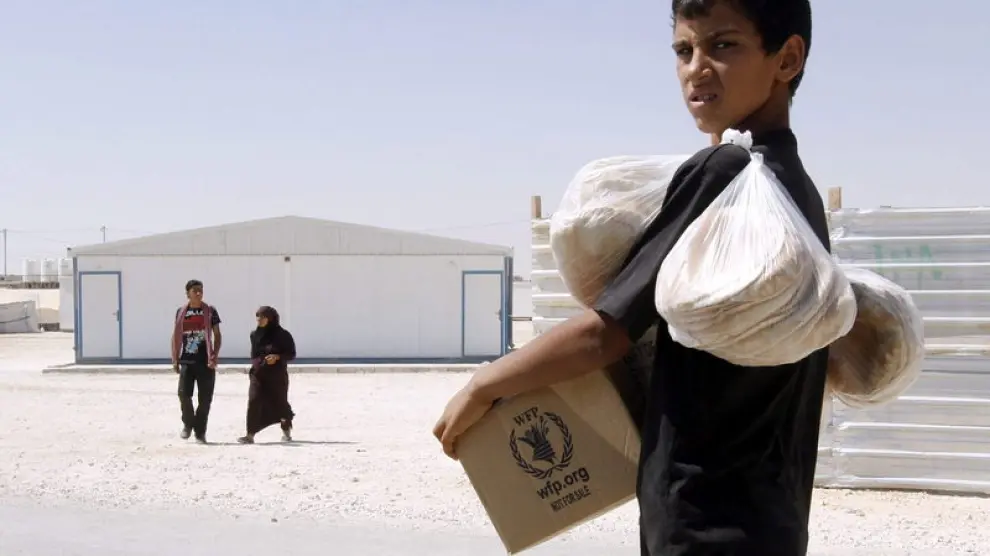 Un refugiado sirio carga con provisiones en un campo de refugiados de Zattari