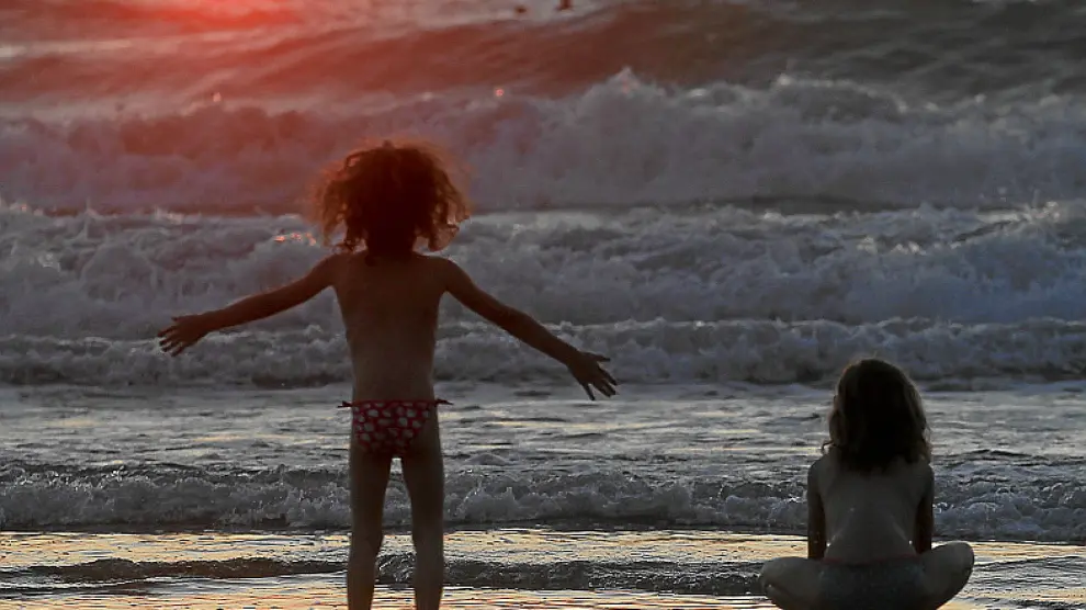 Unas niñas disfrutan del oleaje en la playa de la Zurriola, de San Sebastián, al atardecer