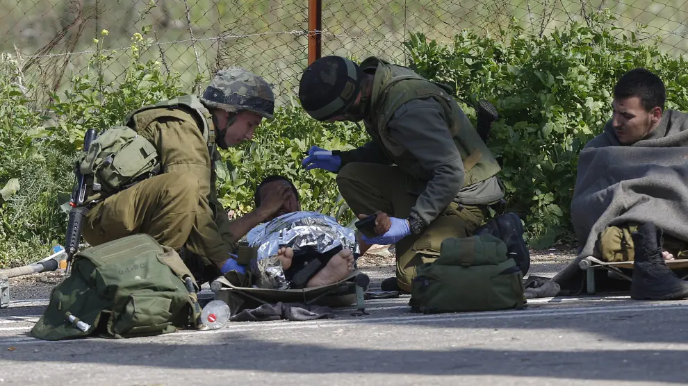 Un soldado isrelí herido recibe atención médica de varios compañeros después de que impactara un misil antitanques en su vehículo cerca de la zona de Har Dov