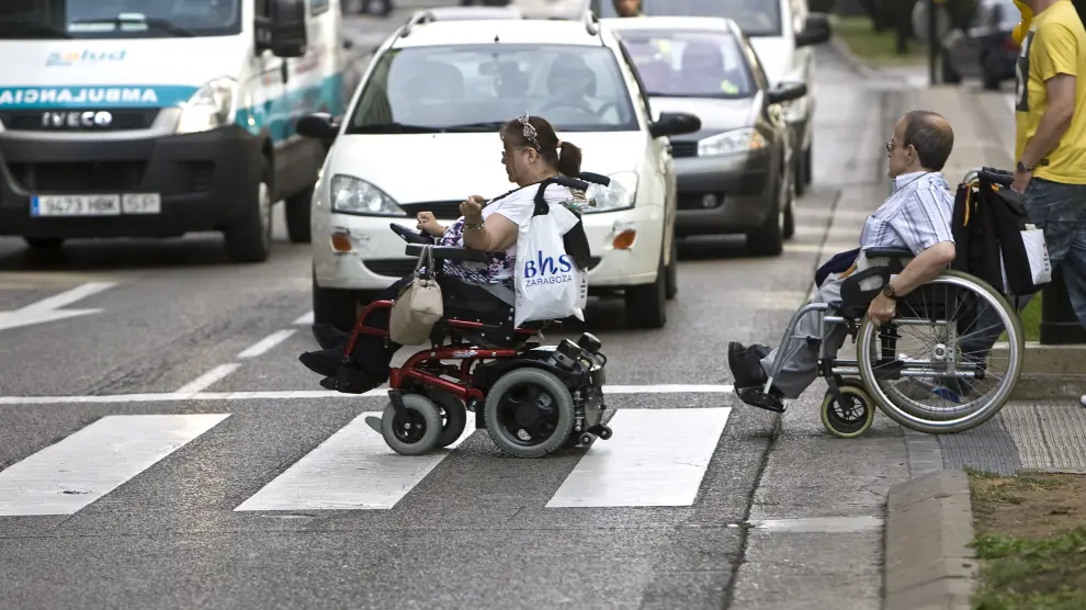 Dos zaragozanos atraviesan un cruce en silla de ruedas