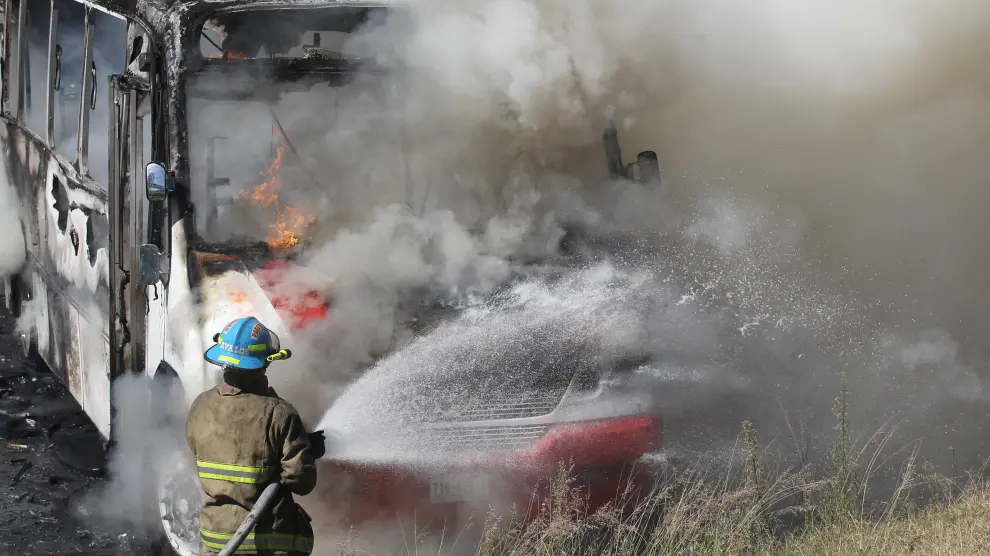 Un bombero apaga uno de los autobuses incendiados en los disturbios de Jalisco.