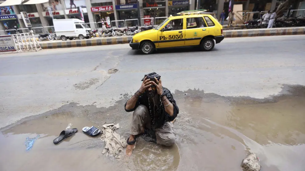 Un hombre intenta refrescarse con un charco que hay en la calle
